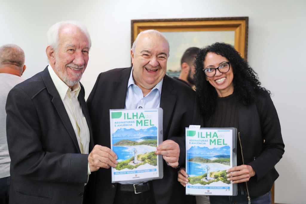 Novo marco regulatório da Ilha do Mel avança com instituição de comitê gestor 4 Participantes sorridentes segurando revistas com a capa do projeto Ilha do Mel, destacando assinaturas e comunicações importantes. Novo marco regulatório da Ilha do Mel avança com instituição de comitê gestor