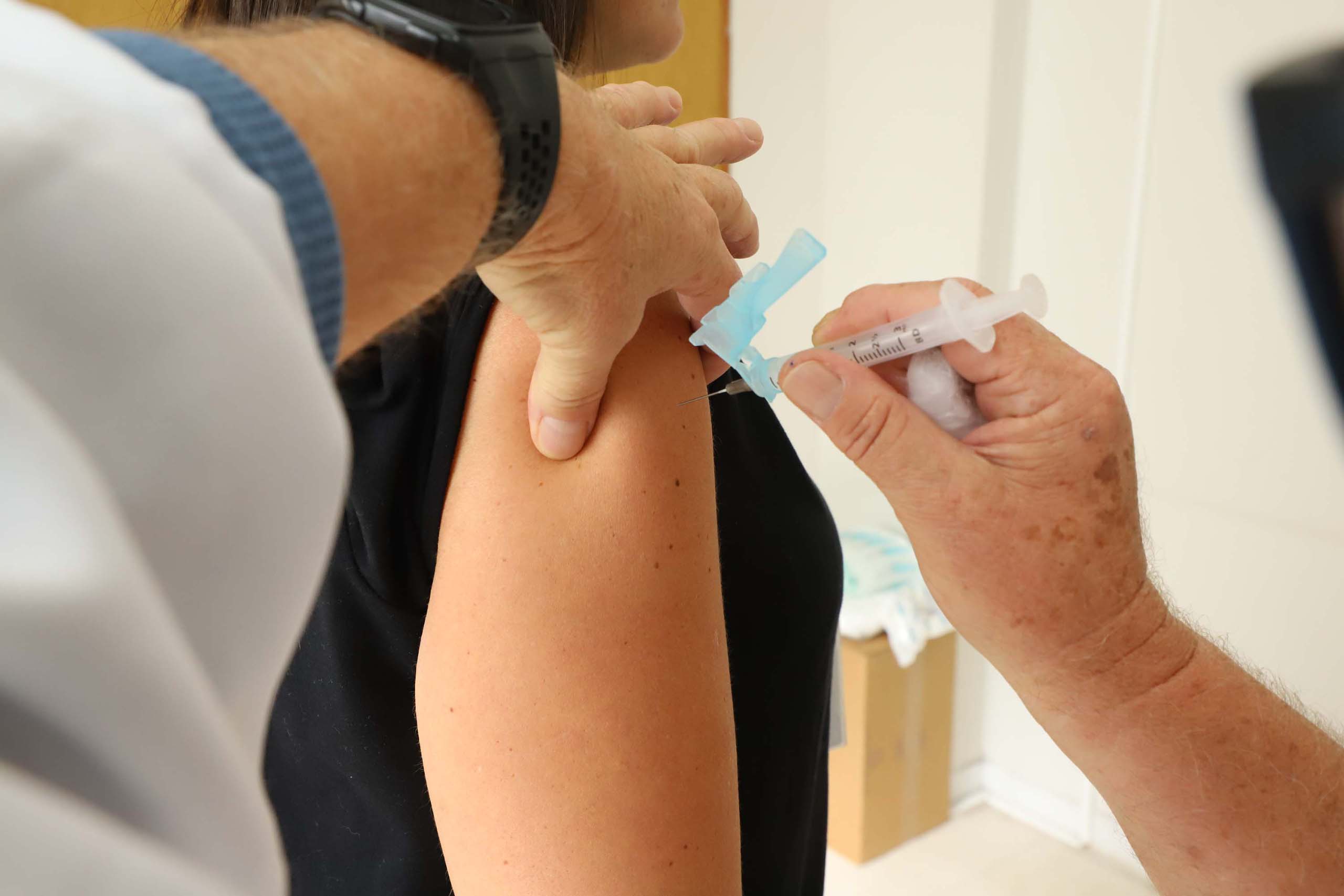 Imagem de vacinação sendo realizada em um braço, mostrando profissionais de saúde administrando a vacina com uma seringa. Dia D de multivacinação no Paraná será no sábado; meta é atingir 300 mil doses aplicadas