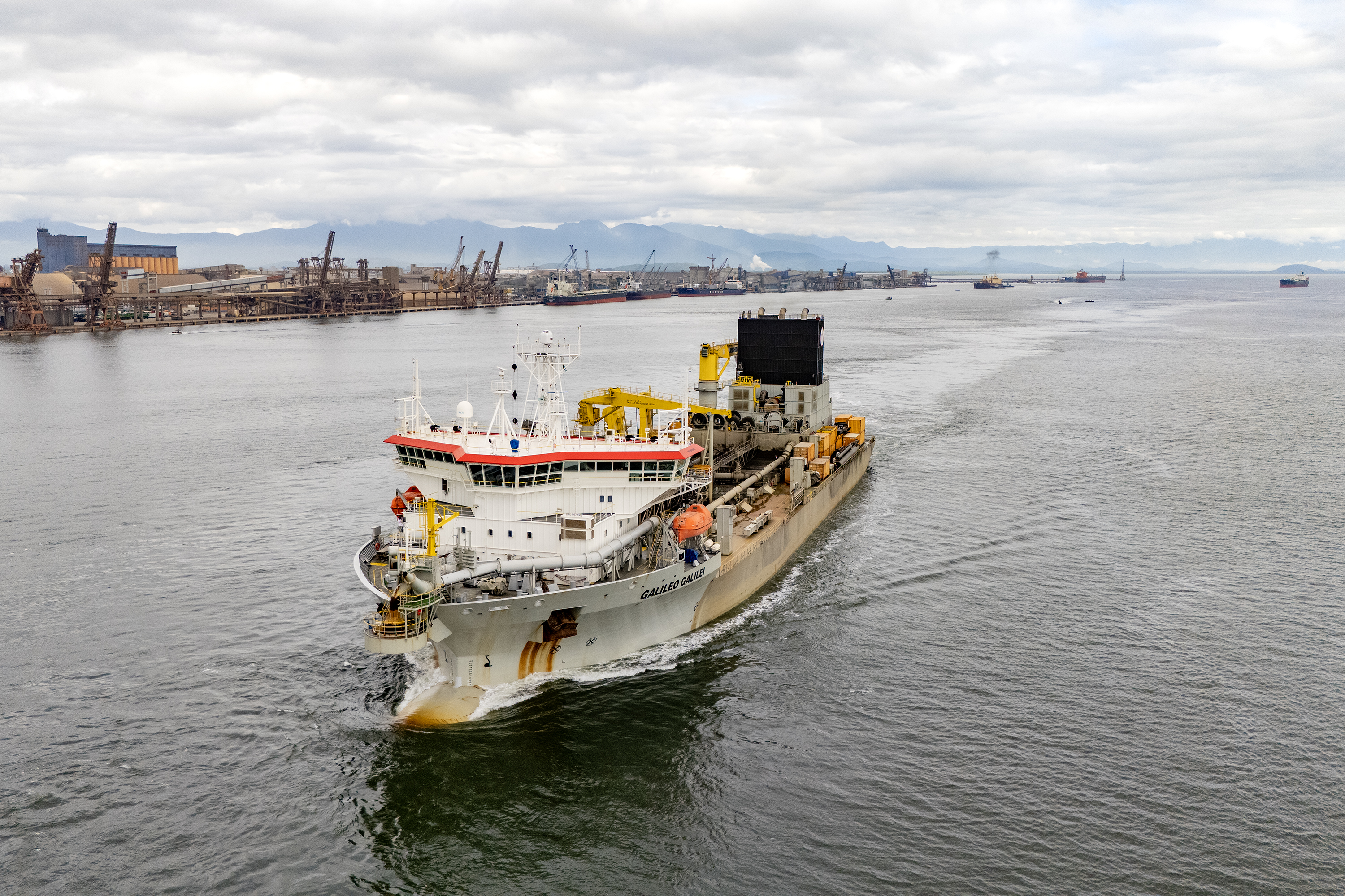 Vista de um navio cargueiro navegando em um porto, destacando a infraestrutura portuária e o comércio marítimo. Portos do Paraná inicia campanha anual de dragagem de manutenção