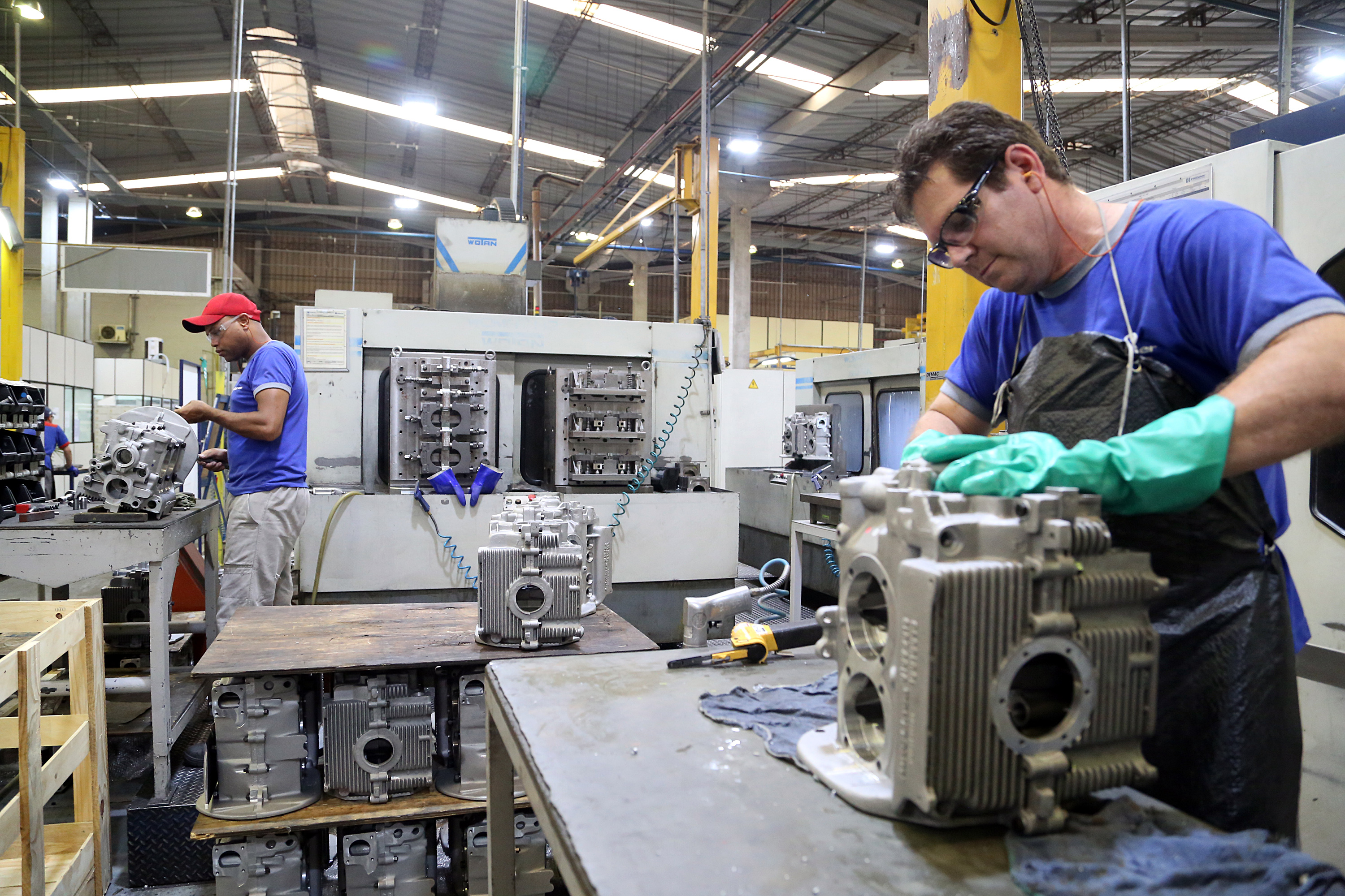 Trabalhadores em uma fábrica montando peças de motores. Ambiente de produção industrial com máquinas e componentes métallicos. 20,5 mil vagas: semana começa com várias oportunidades de emprego no Paraná