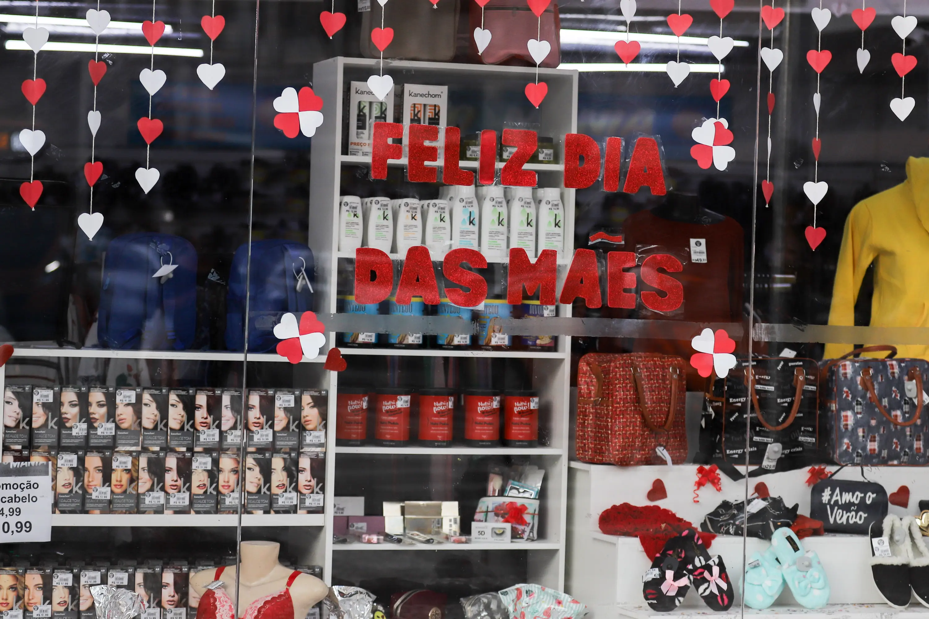 Vitrine decorada para o Dia das Mães, com a mensagem 'Feliz Dia das Mães' em destaque, coroada por corações vermelhos e brancos. Exposição de produtos variados para presentes. Dia das Mães: Procon-PR dá dicas para não ter surpresas na compras de presentes