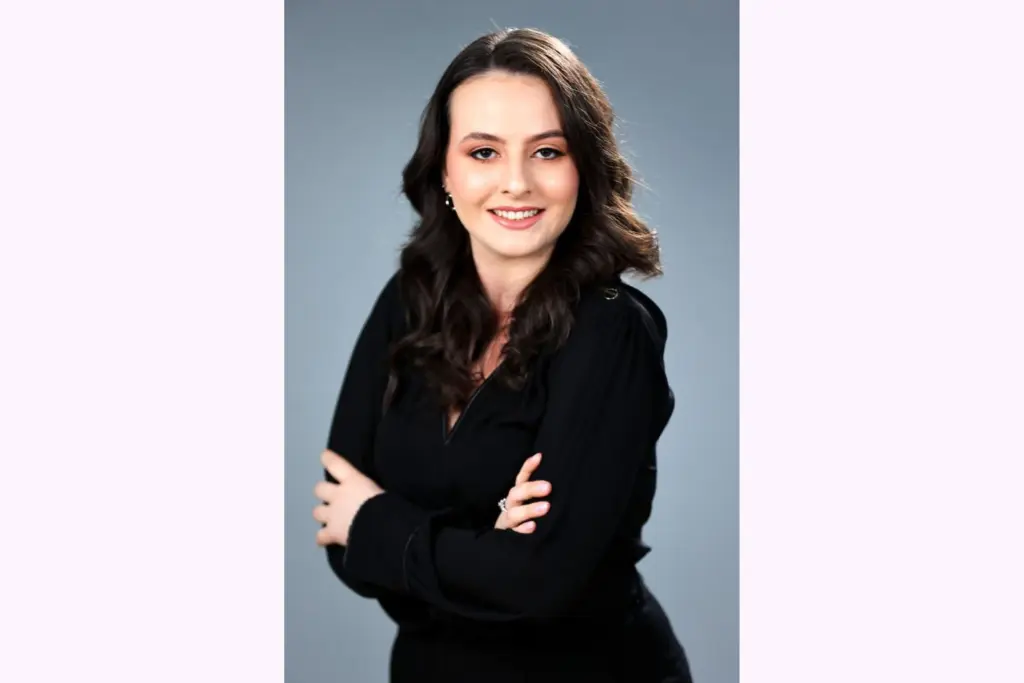 Retrato de uma mulher jovem com cabelo castanho, sorriso acolhedor e vestindo roupa preta, na frente de fundo cinza, ideal para conteúdo de moda ou beleza. Lei da Desburocratização: o que muda para o cidadão com a Lei n.º 13.726/2018