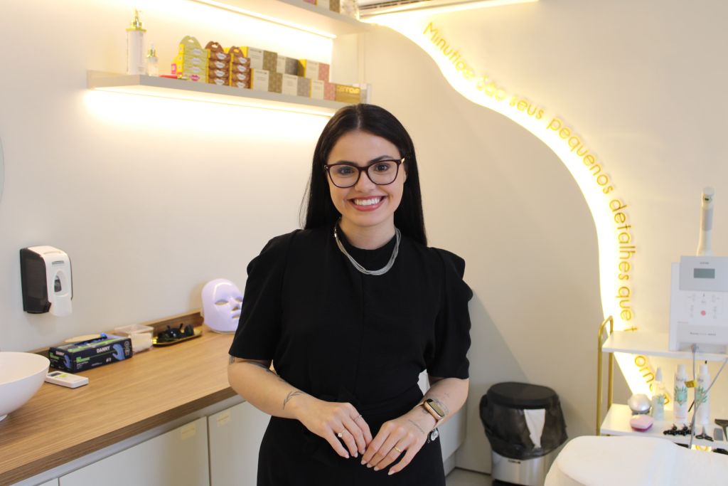 IMG_0174 (1) Mulher sorridente com óculos e roupa preta, em ambiente de clínica ou consultório odontológico, com decoração moderna e iluminação acolhedora. Clínica I’M: Isabele Monte e sua carreira de maquiadora até à gestão de uma clínica multidisciplinar